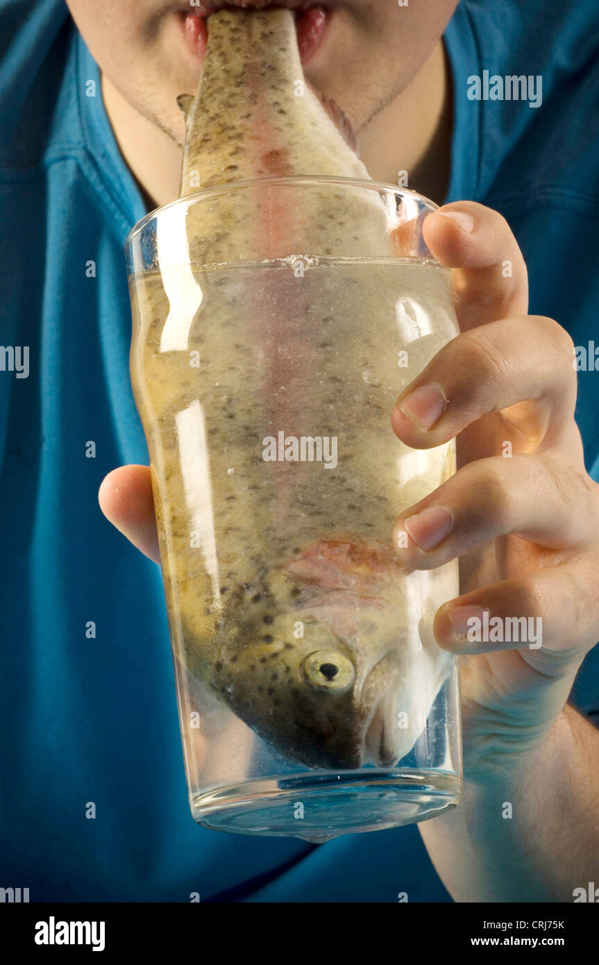 Un cocktail di pescoso. Giovane uomo drink da un bicchiere di acqua in cui vi è un pesce. L'acqua, l'elisir di lunga vita e un pesce, la fonte primaria di omega-3, considerata come un importante beneficio per la salute. Foto Stock