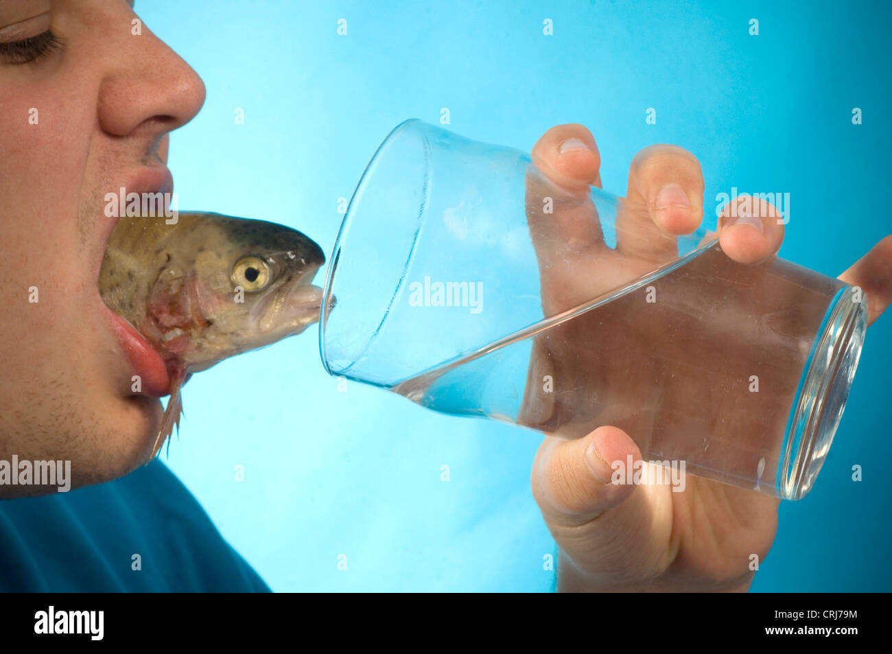 Un cocktail di pescoso. Giovane con un pesce nella sua bocca e beve un bicchiere d'acqua. L'acqua, l'elisir di lunga vita e un pesce, la fonte primaria di omega-3, considerata come un importante beneficio per la salute. Foto Stock