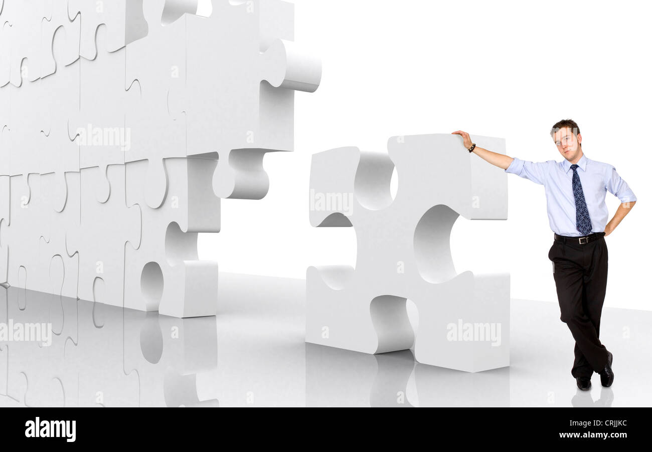 Imprenditore selfconfidently appoggiata contro un gigantesco pezzo di puzzle in un puzzle incompiuto parete Foto Stock