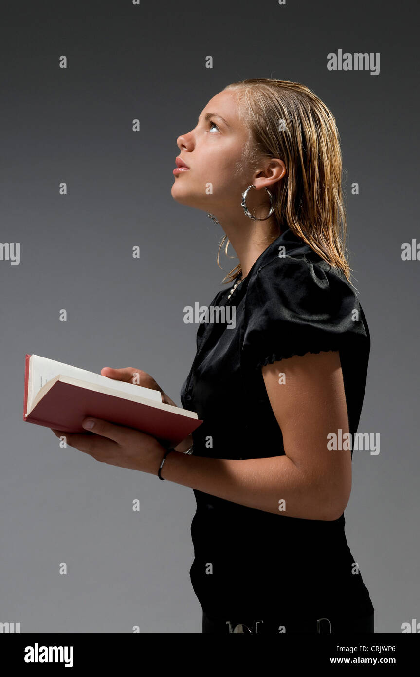 Elegante bionda ragazza in piedi con un libro in mano cercando perso nel pensiero Foto Stock