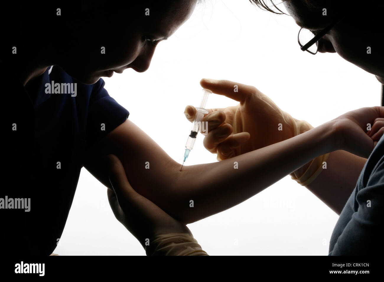 Una silhouette di un medico con una siringa per prelevare un campione di sangue dal braccio di un giovane paziente femmina. Foto Stock