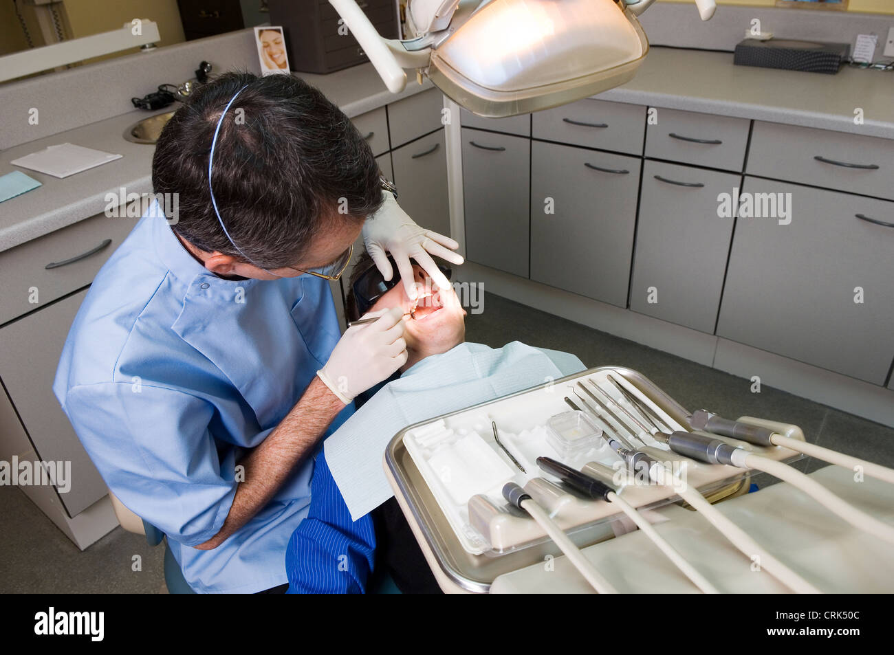 Dentista di indossare occhiali di sicurezza e la maschera di bocca esamina i denti del giovane paziente di sesso maschile, anche indossando speciali occhiali di protezione. Foto Stock