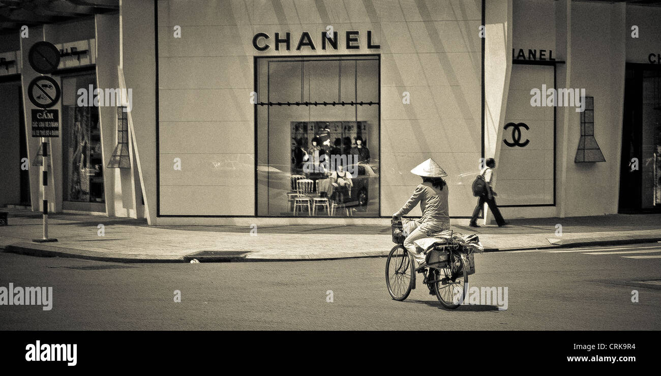 Bel contrasto tra questa tipica vietnamita di equitazione donna la sua bicicletta e il lusso elevato Chanel store in Dist.1, Ho Chi Minh, Vietnam Foto Stock