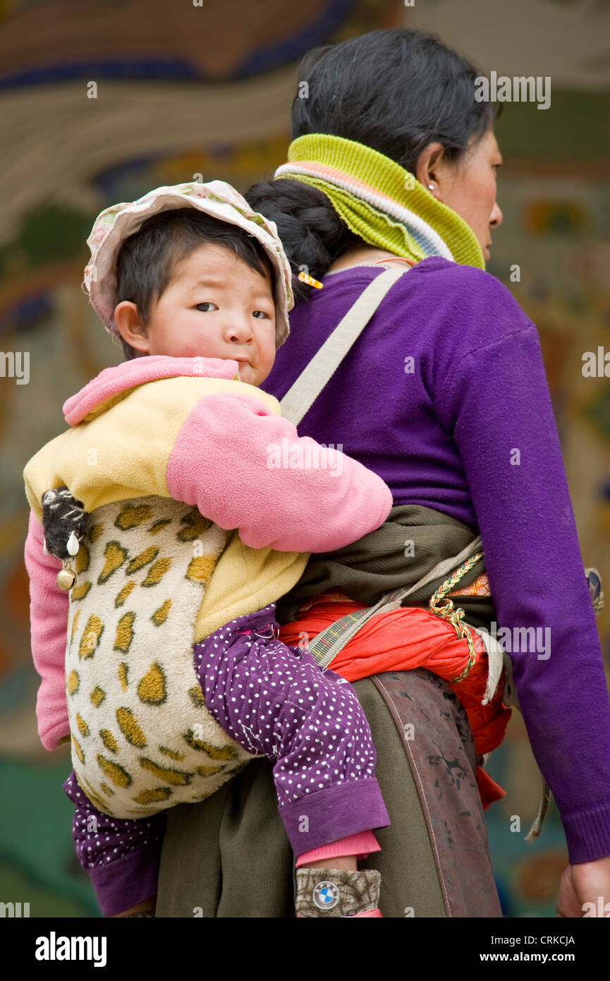 Un tibetano madre cinese che porta il suo bambino sulla schiena presso il monastero di Labrang a Xiahe. Foto Stock