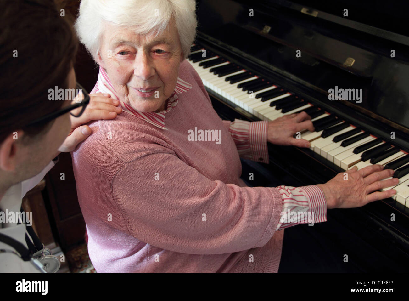 Medico guarda la donna più anziana suonare il pianoforte Foto Stock
