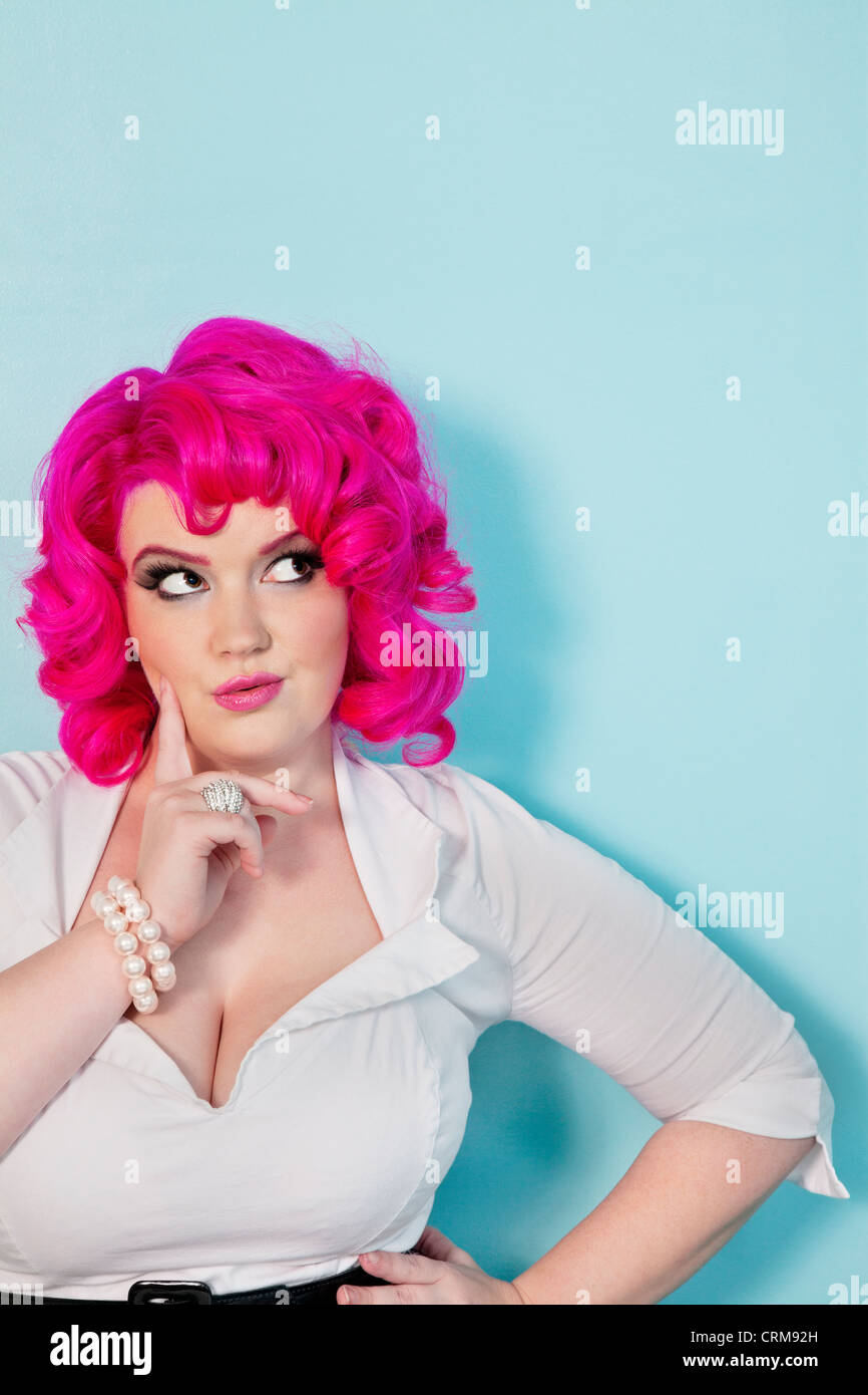 Giovane donna fantasticando con il dito sulla faccia su sfondo colorato Foto Stock