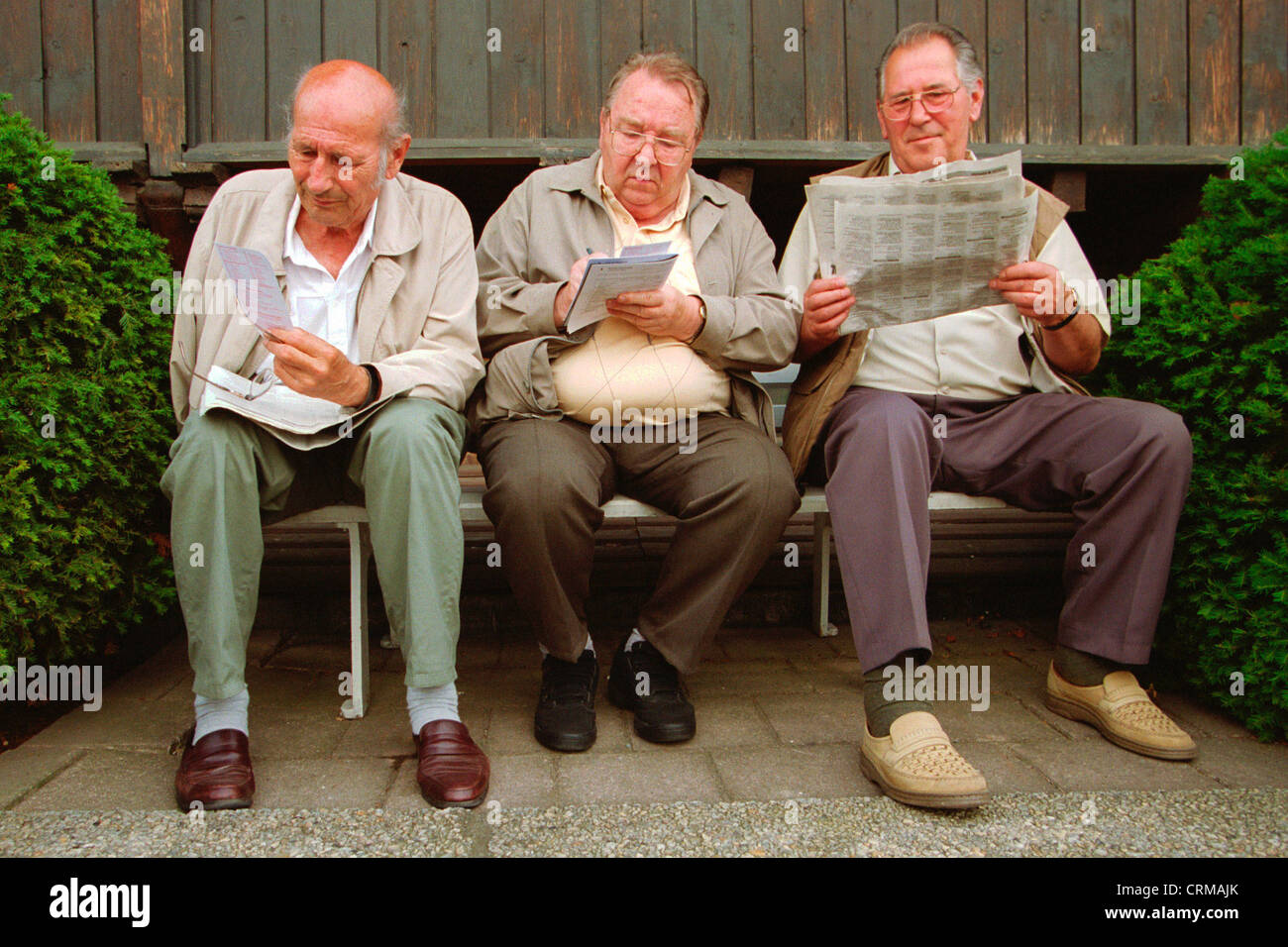 A Dresda, tre pensionati seduti su una panchina e leggere Foto Stock