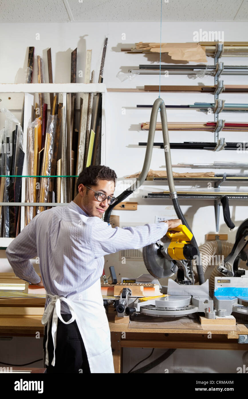 Ritratto di un giovane uomo che guarda indietro mentre utilizzando una sega circolare in officina Foto Stock