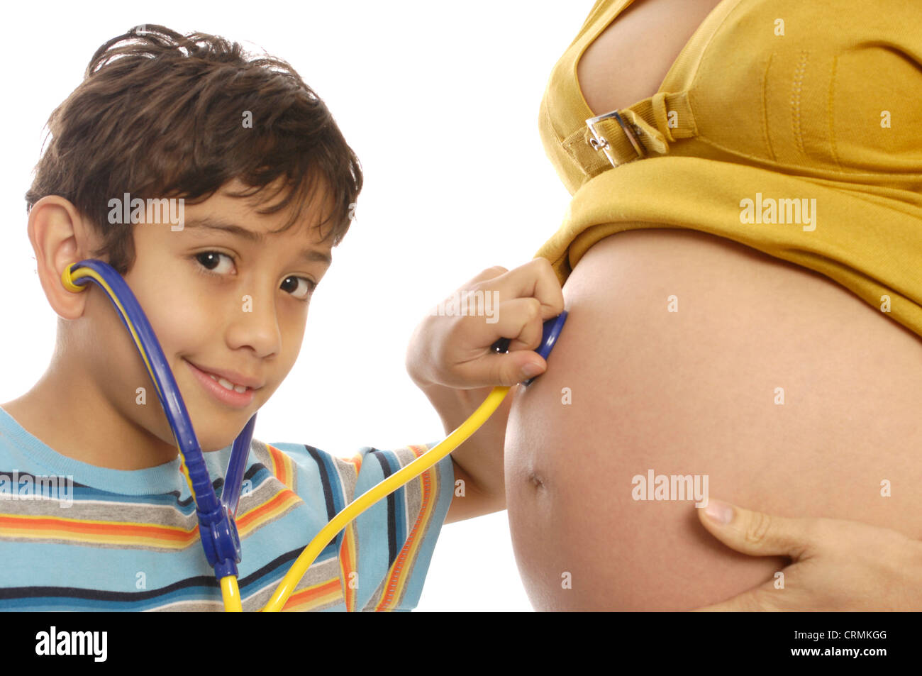 Un giovane ragazzo che finge di ascoltare il suo madri incinte" stomaco con un giocattolo stetoscopio Foto Stock