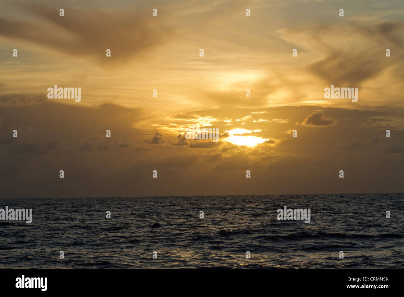 Un cuore a forma di cloud è evidenziato da un tramonto sull'oceano. Foto Stock