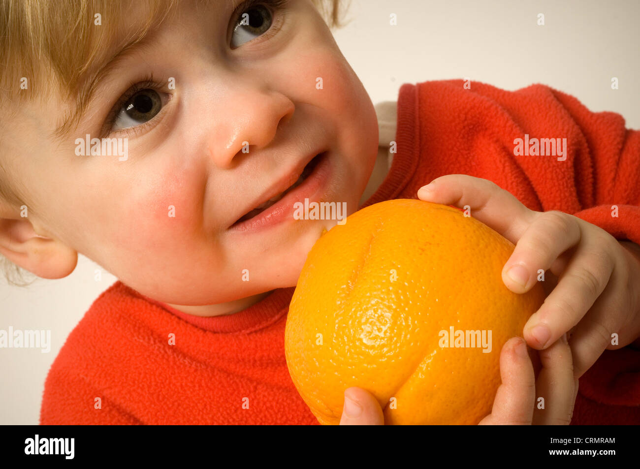 Un giovane bambino mordere nella pelle amaro di un arancione. Foto Stock