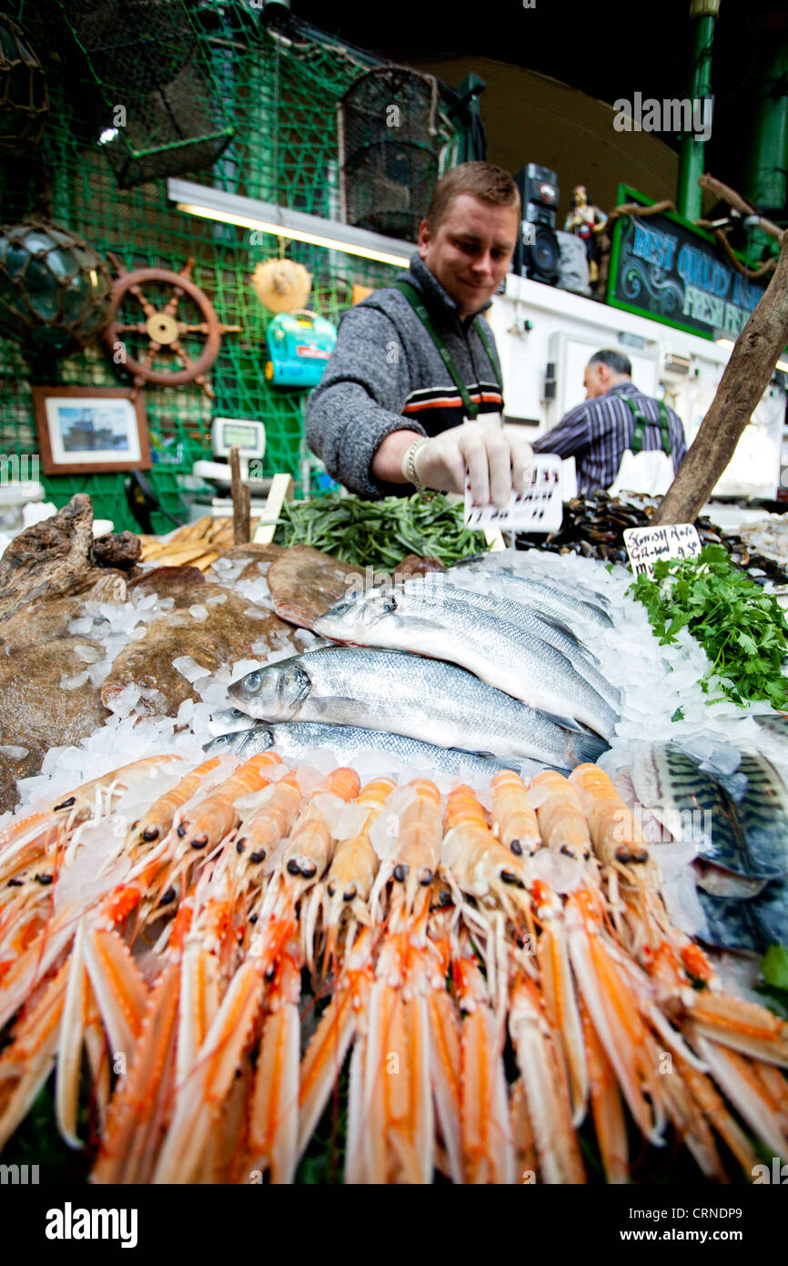 Un pescivendolo posa di tonno fresco e pesce di shell in vendita da uno stallo nel mercato di Borough. Foto Stock