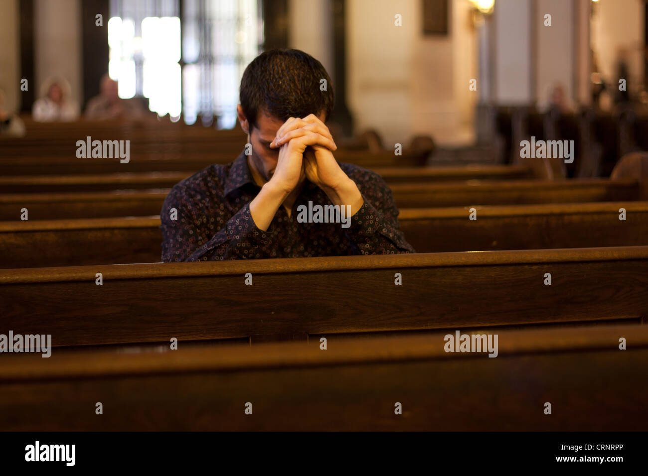 Giovane uomo in preghiera nella chiesa sul banco di lavoro Foto Stock