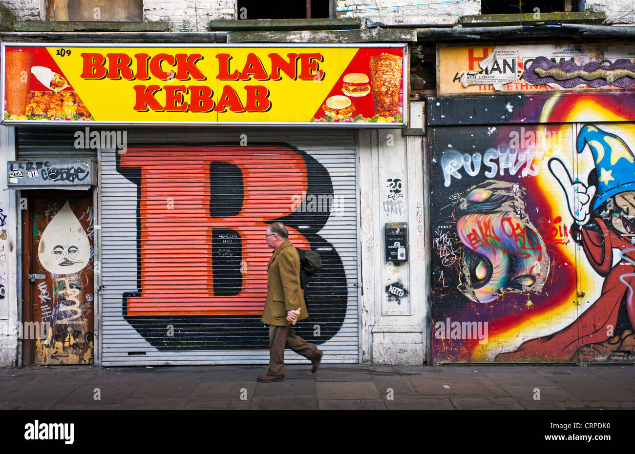 Un uomo a piedi lavoro vetrine passato coperto di graffiti su Brick Lane nell'East End di Londra. Foto Stock