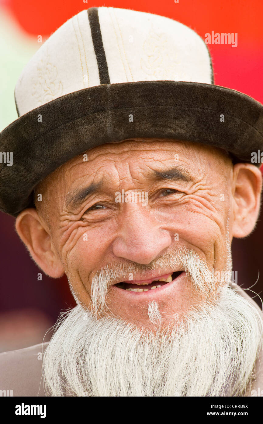 Un anziano Uyghur uomo cinese pongono per la fotocamera in abiti tradizionali al mercato locale nella piccola cittadina di Upal, Cina. Foto Stock