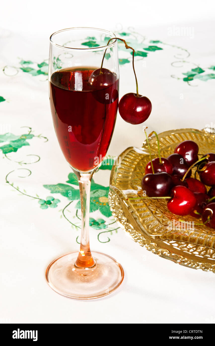 Derivava wineglass contenenti succo di frutta e due ciliege rosse sul cerchio su un verde applique tovaglia. Foto Stock