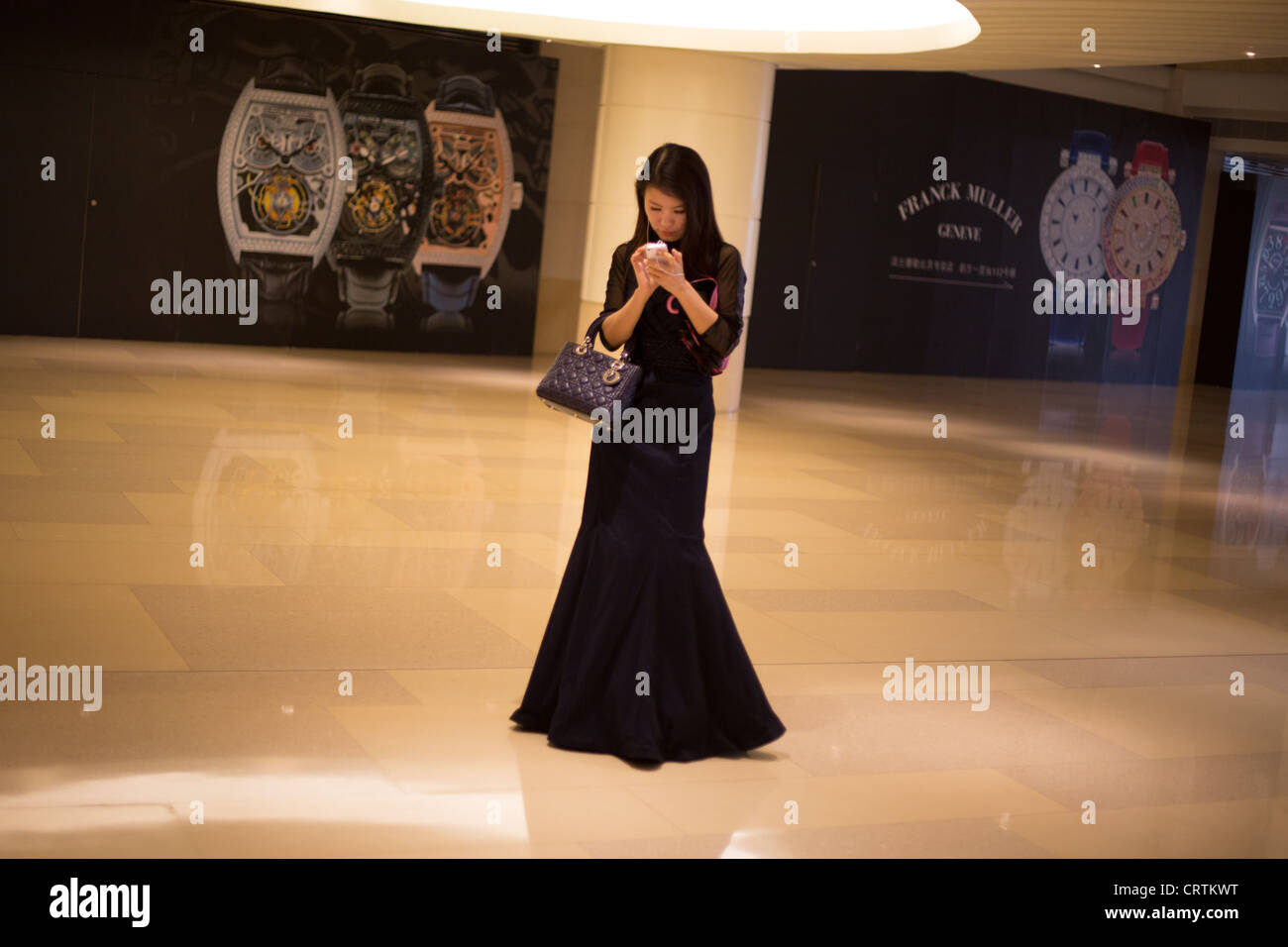 Donna che indossa la sera abito, con telefono mobile, in un centro commerciale per lo shopping, a Pechino, Cina Foto Stock