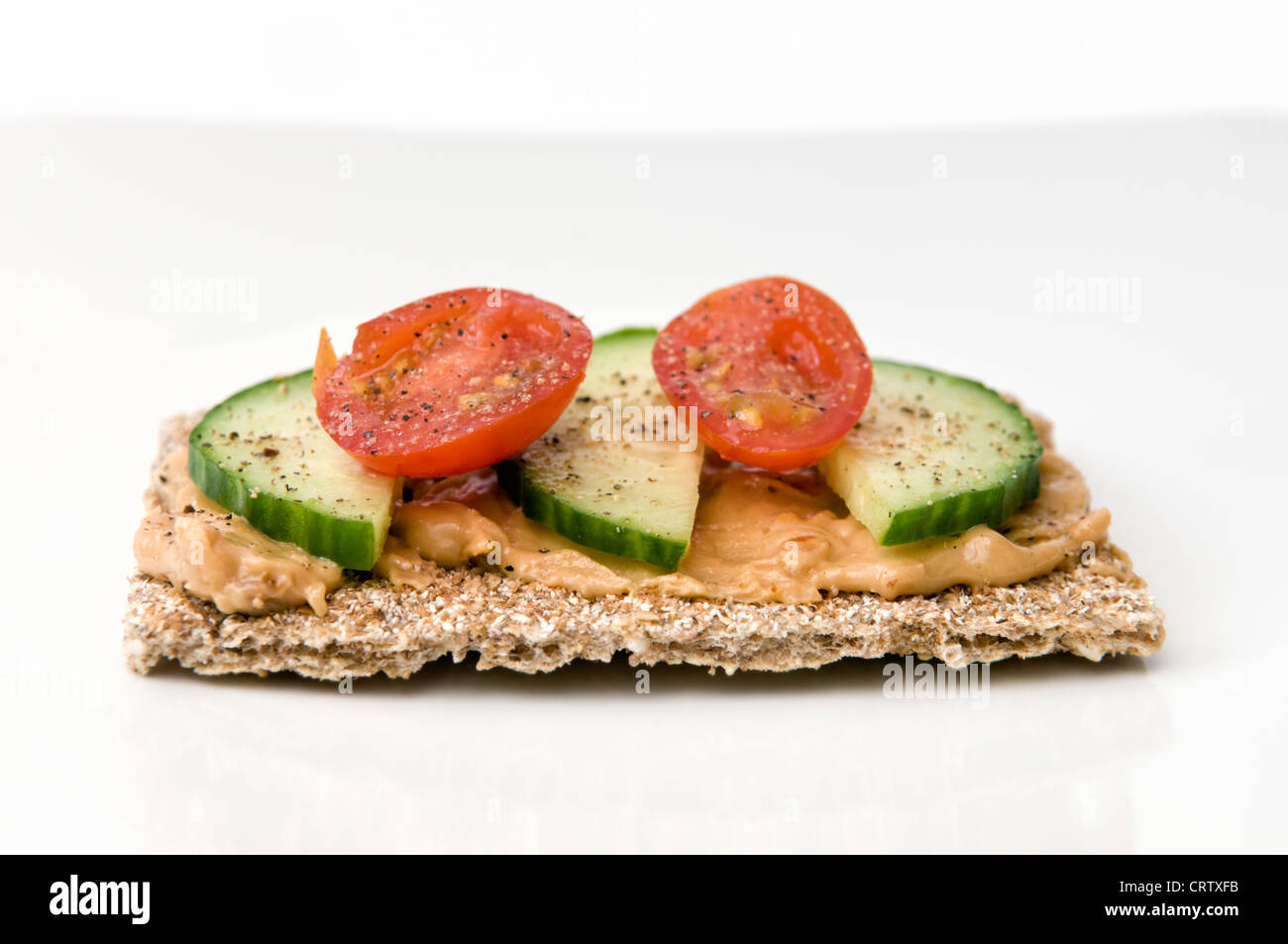 Crostini con burro di arachidi, fette di cetriolo e pomodoro su piastra bianca con il condimento sulla parte superiore Foto Stock