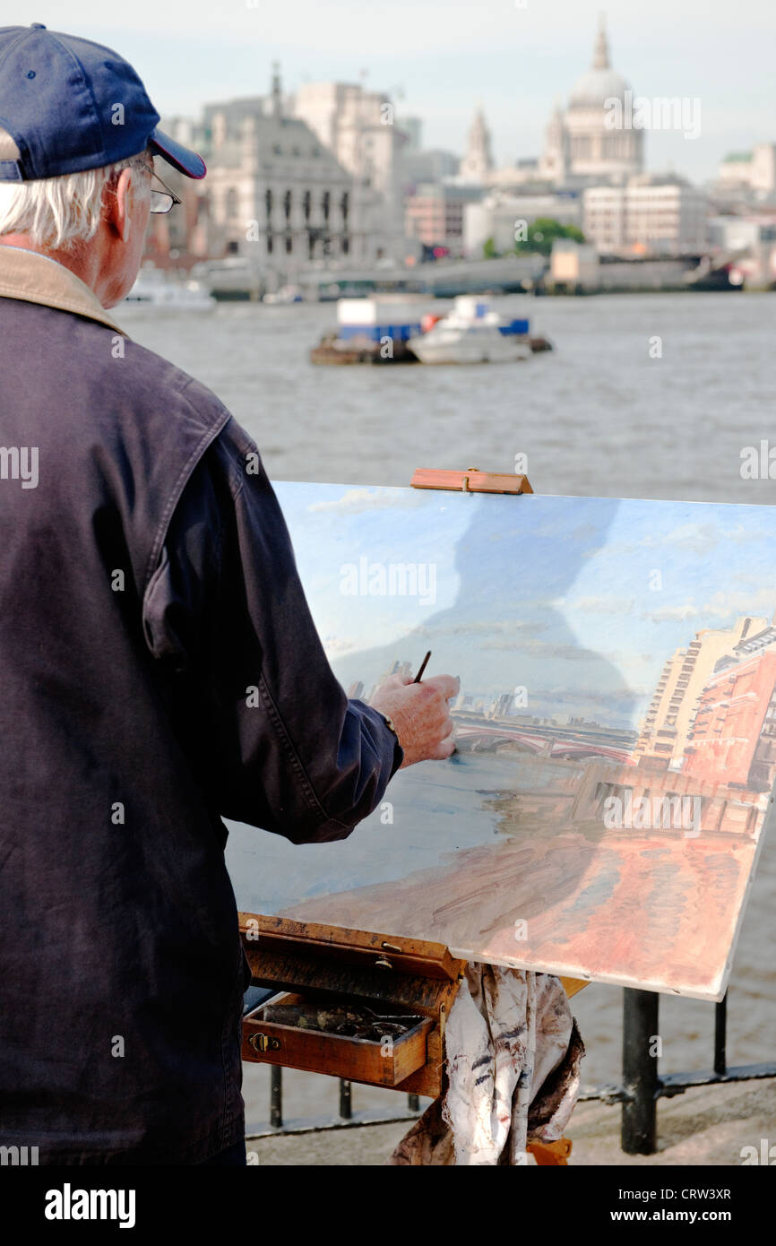 Un maschio dai capelli grigi artista dipinge il panorama della città di Londra skyline dalla banca del sud del Tamigi in una limpida giornata estiva Foto Stock