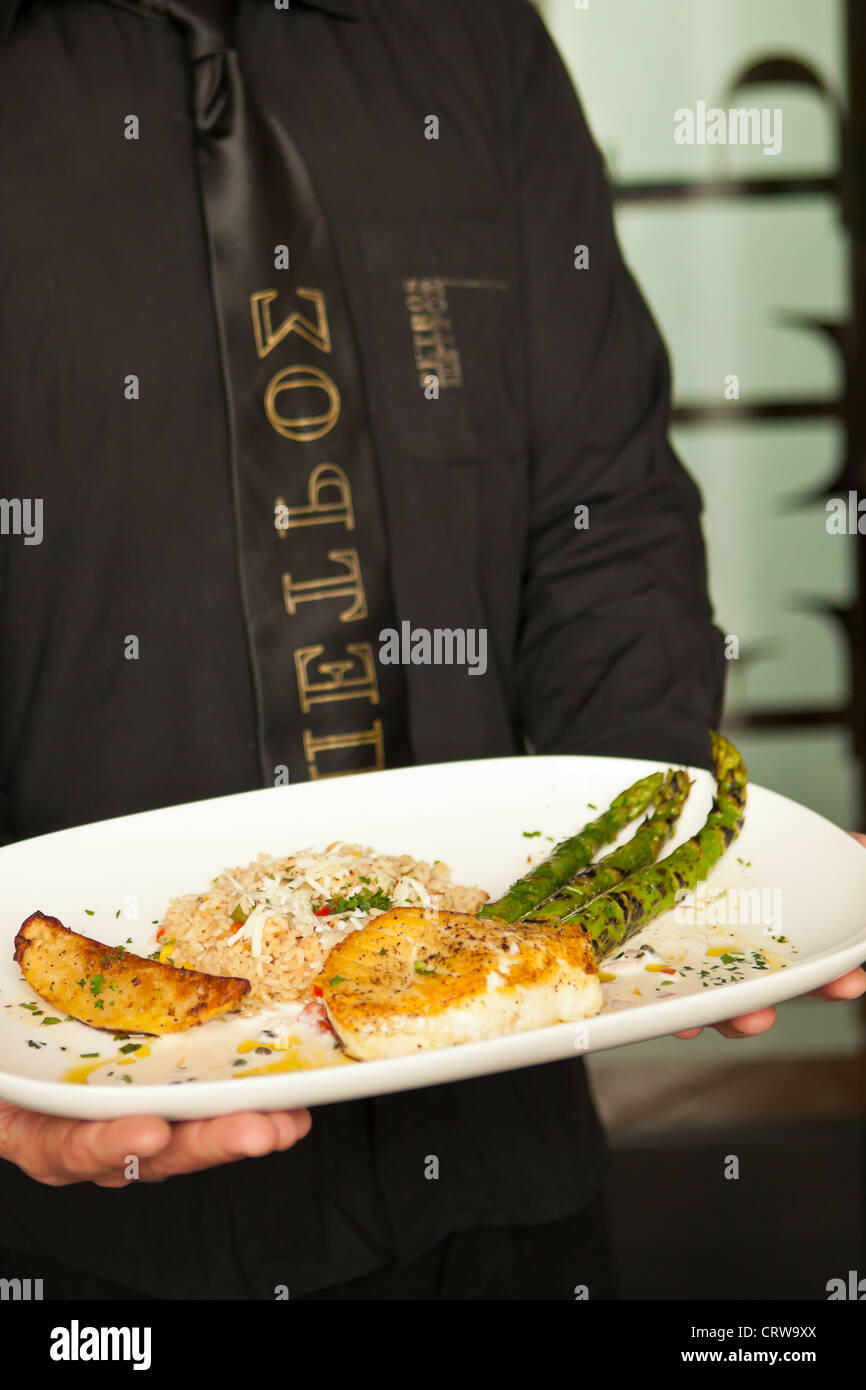 Uomo che serve saltata di branzino con asparagi, Petros ristorante greco, Santa Barbara, California Foto Stock