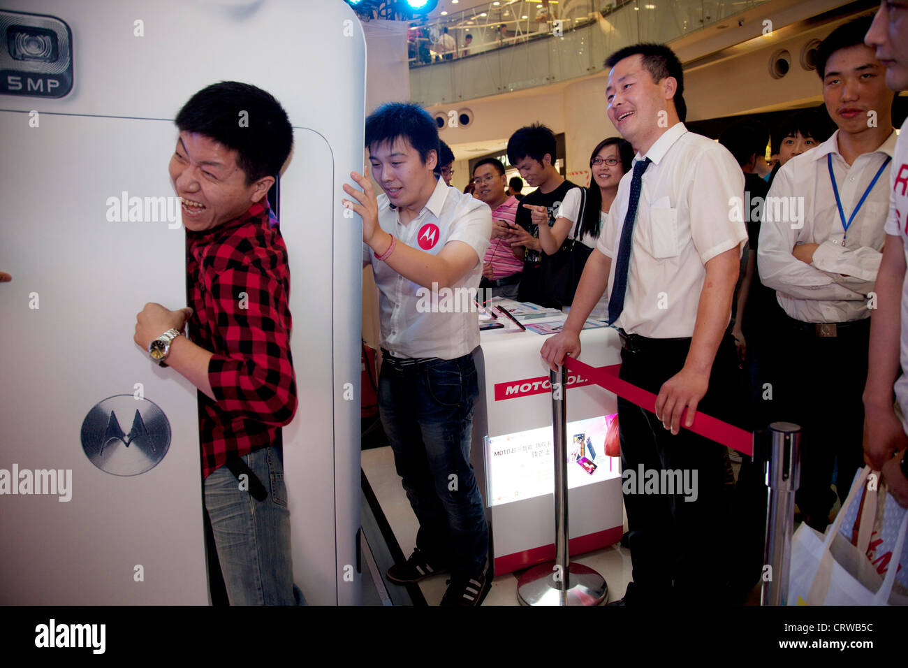 Shopper cerca di vincere un premio dalla spremitura attraverso un grande telefono cellulare Motorola. Joy City shopping mall, Xidan, Pechino. Foto Stock