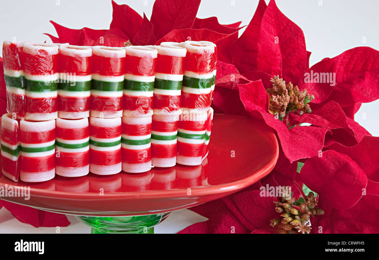 Ribbon candy impilati sul piatto di caramelle con poinsettias di nuovo sfondo bianco. Foto Stock