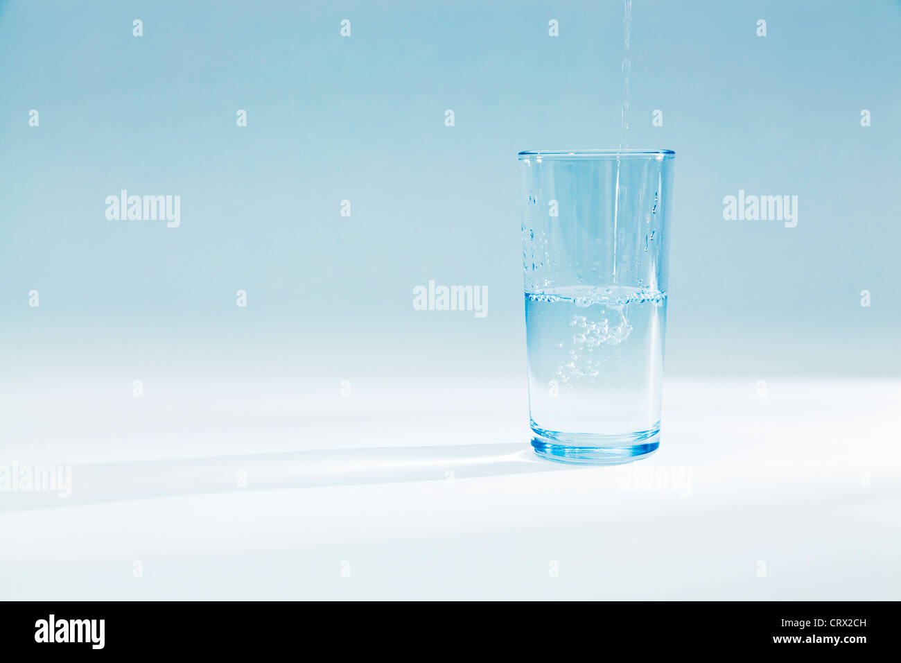 Acqua versando in un pieno per metà un bicchiere di vetro in una luce blu Foto Stock