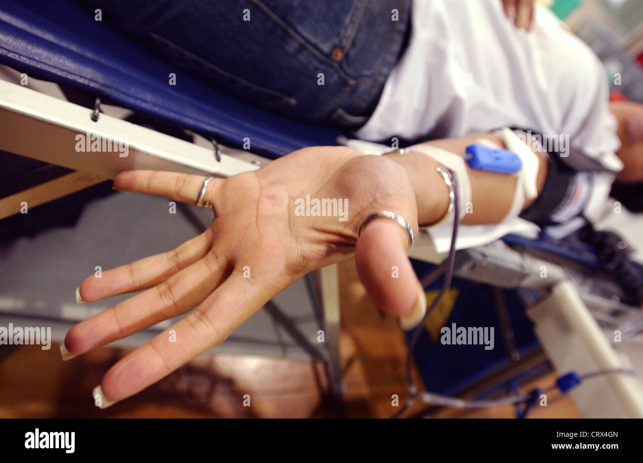 Giovane donna donatore con un pugno aperto come il sangue scorre attraverso l'ago e il tubo in un sacchetto di contenimento. Foto Stock