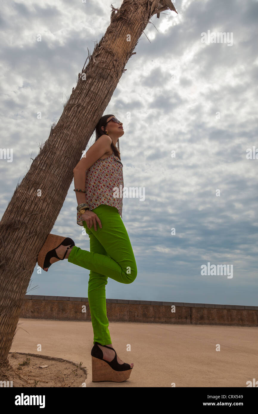 Bellissimo modello in appoggio su di un albero di palma e guardando il cielo sulla spiaggia di Malvarrosa (Valencia) Foto Stock