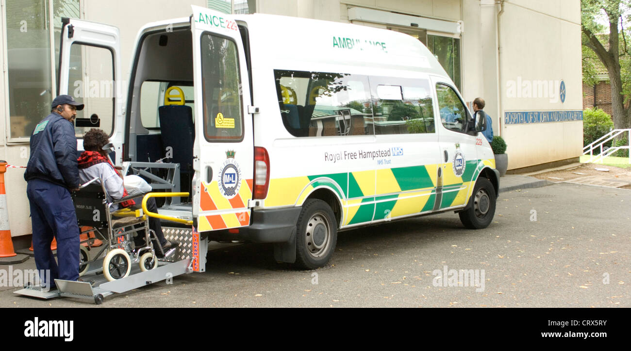 Un paziente su sedia a rotelle è issato in una ambulanza da un personale paramedico. Foto Stock
