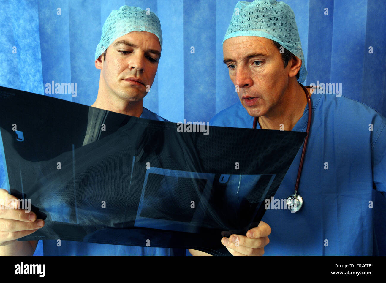 Due chirurghi che indossa blu tappi chirurgico e gli abiti, la revisione di un paziente di raggi x. Foto Stock