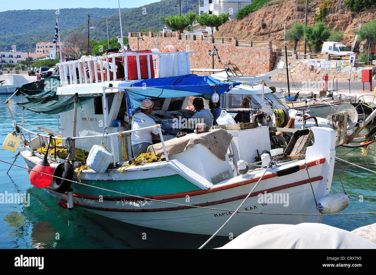 Barca da pesca con pescatori a bordo legato fino alla banchina del villaggio di Milos sull'isola di Agistri, Isole Saroniche, Grecia Foto Stock