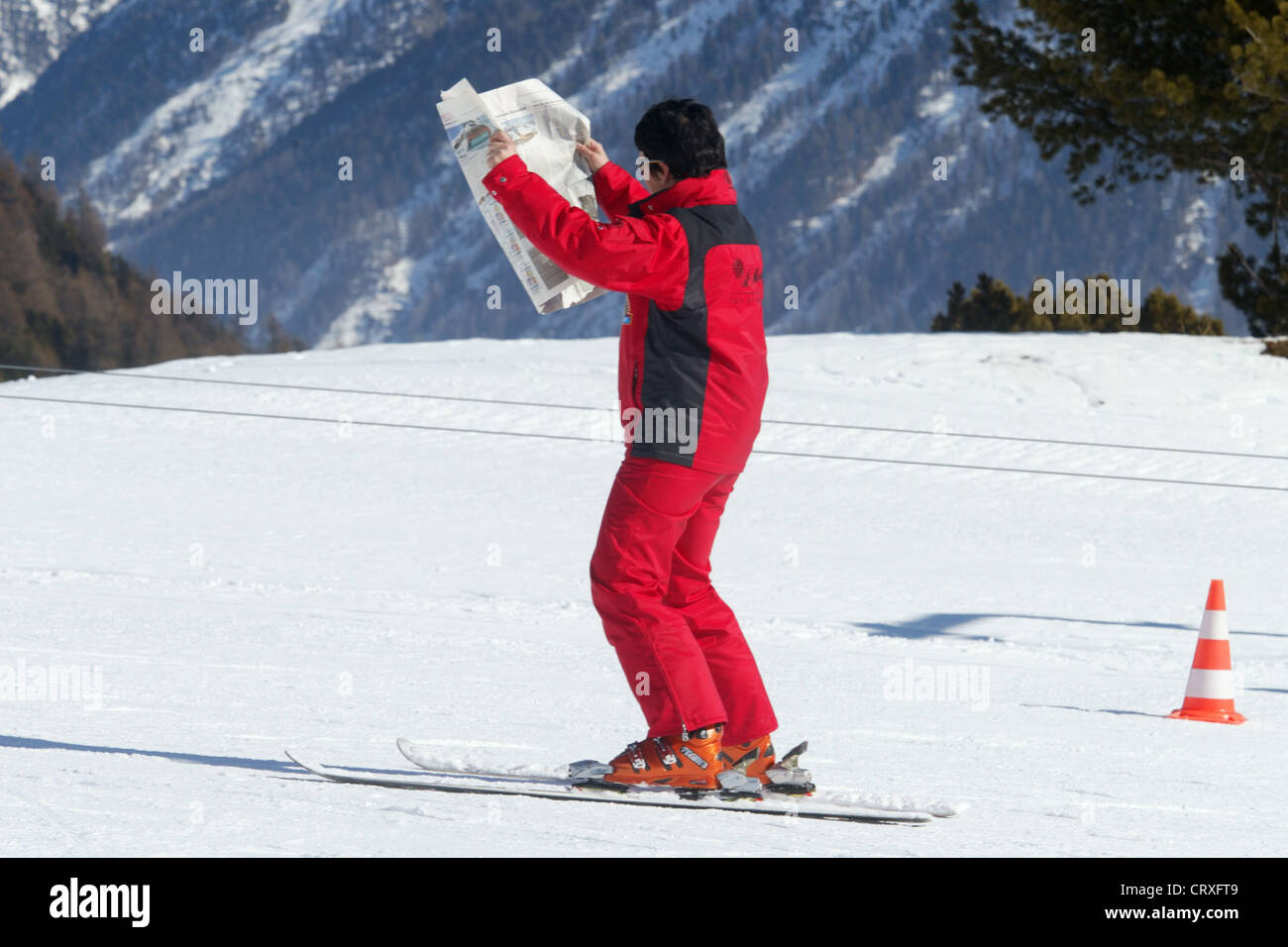 Istruttore legge il giornale mentre lo sci sulle piste da sci Foto Stock