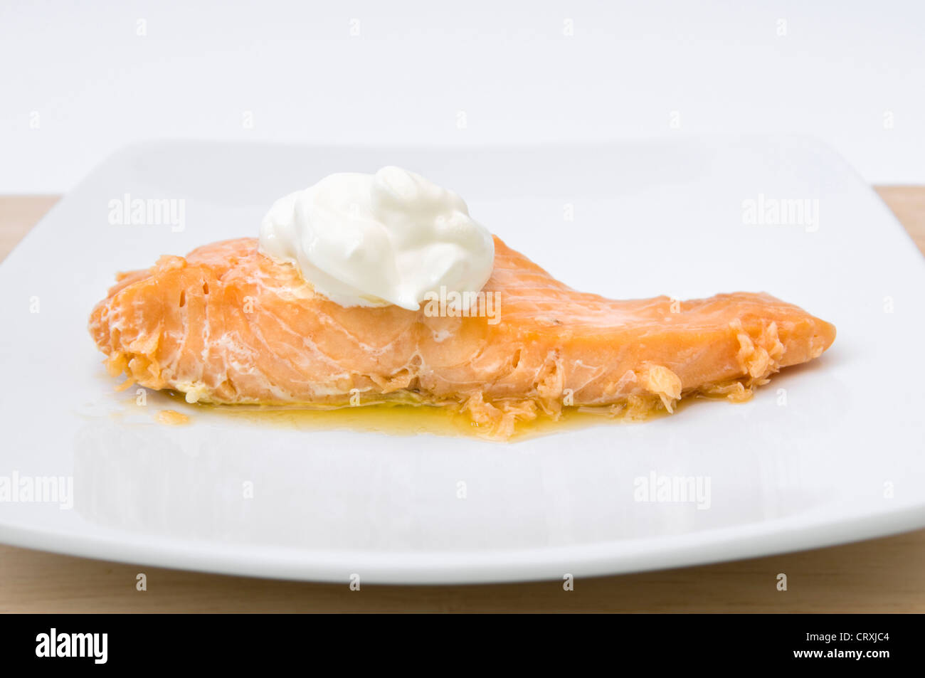 Il salmone cotto con ciuffo di crème fraiche e burro fuso sulla piastra bianca Foto Stock
