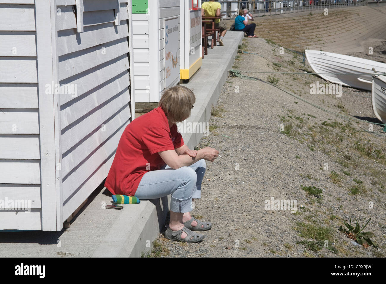 Regno Unito donna seduta sul passo concreto di fumare una sigaretta nella luce del sole Foto Stock