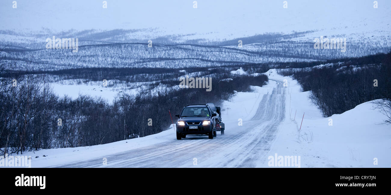 Auto con traino di un rimorchio motoslitta attraverso il deserto artico al calar della sera da Kilpisjarvi sul percorso dalla Norvegia in Finlandia Foto Stock