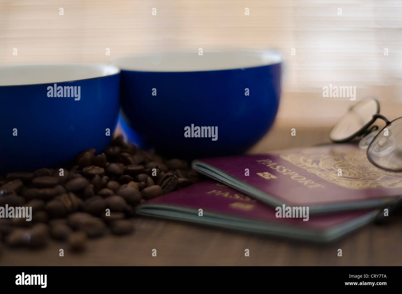 Il piano portapaziente in scena con due blu scuro tazze per il caffè con i chicchi di caffè con due passaporti britannici in legno scuro di quercia del piano portapaziente. Foto Stock
