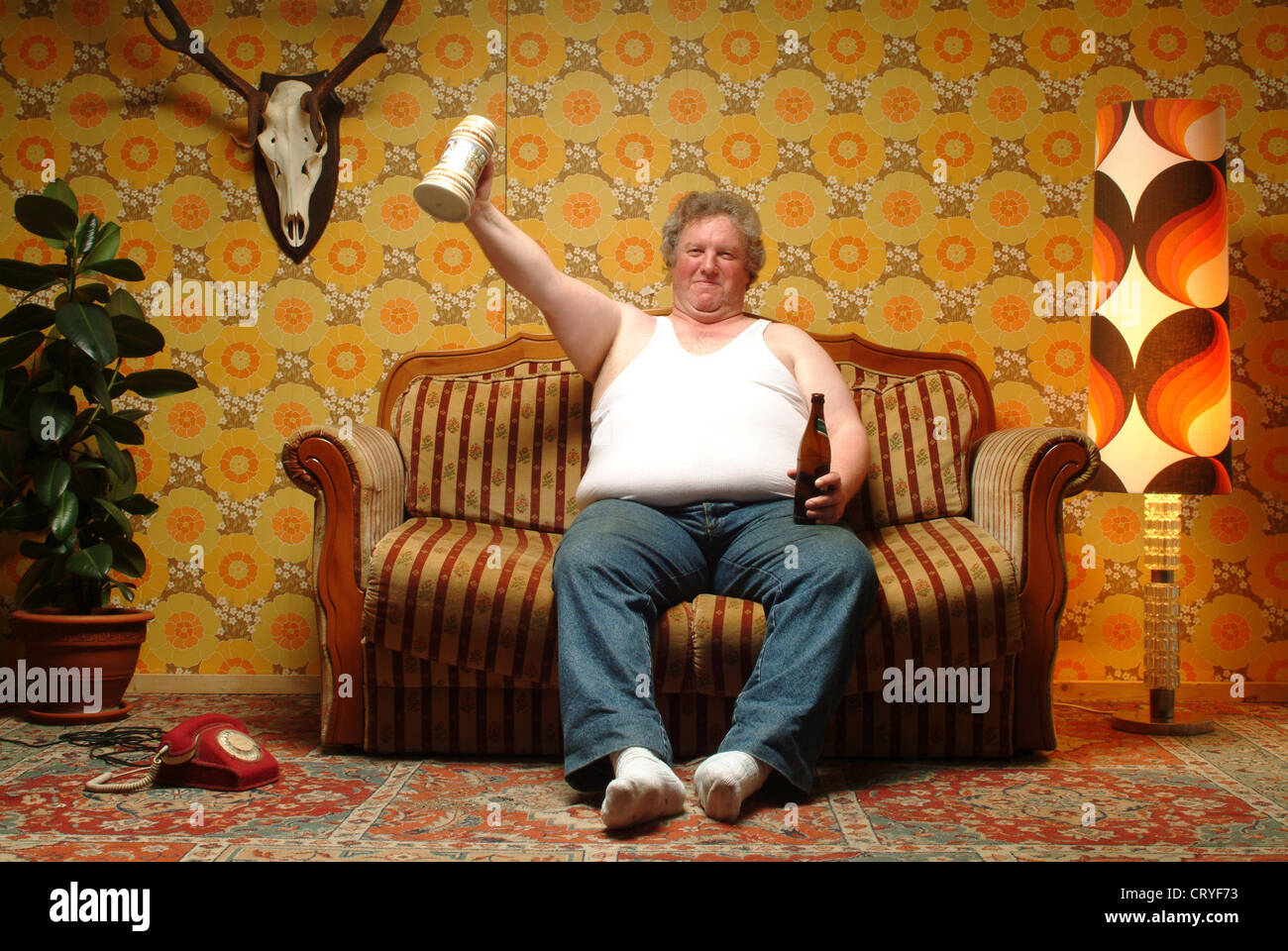 Un uomo grasso seduto sul divano con la birra Foto stock - Alamy