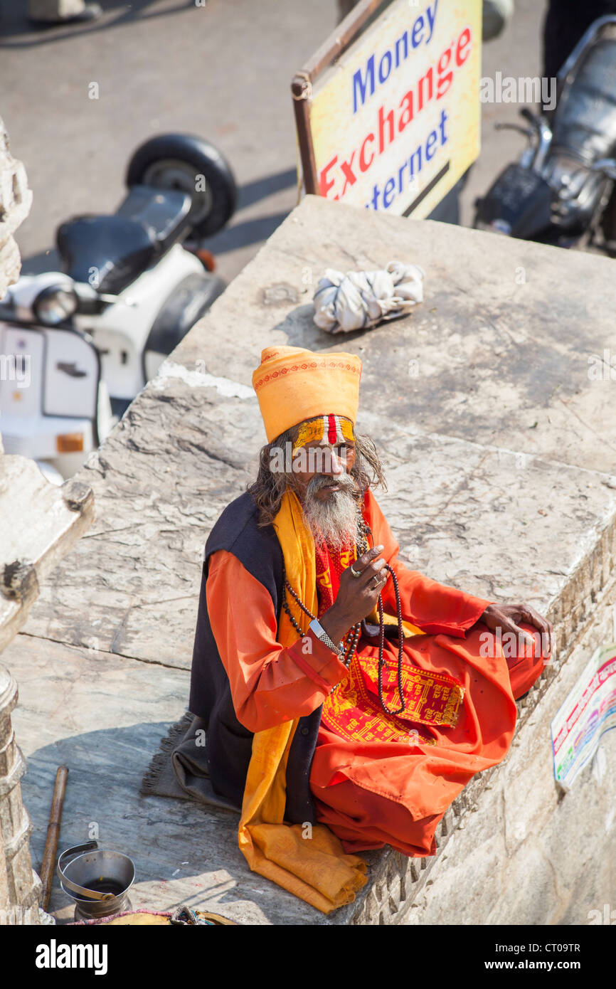 Sadhu, Indù indiano santo uomo, vestito in tradizionali abiti dello zafferano seduta dando una benedizione al di fuori del tempio Jagdish in Udaipur, Rajasthan, India Foto Stock