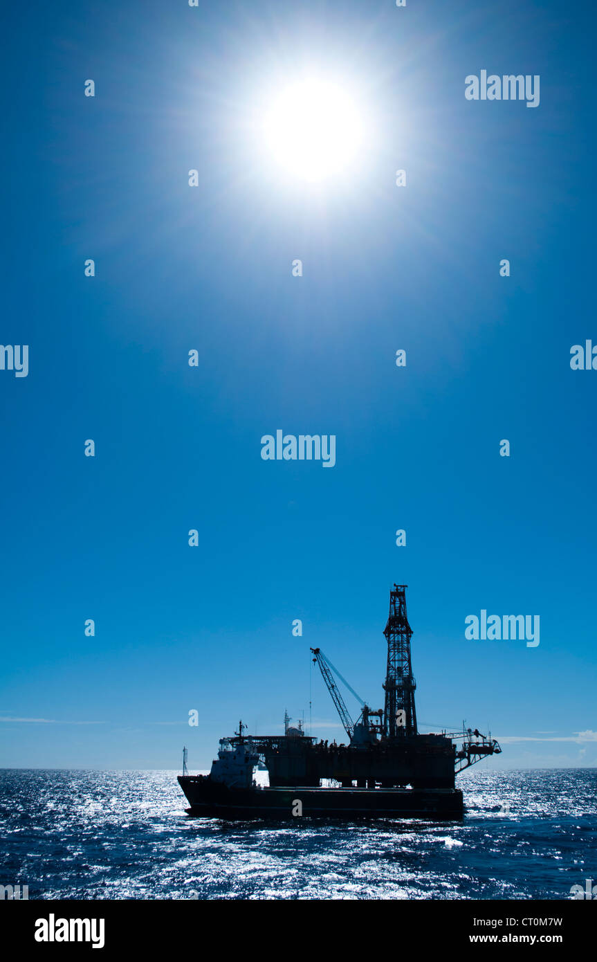 Silhouette di un olio impianto di perforazione offshore con barca di alimentazione lungo il lato. Foto Stock