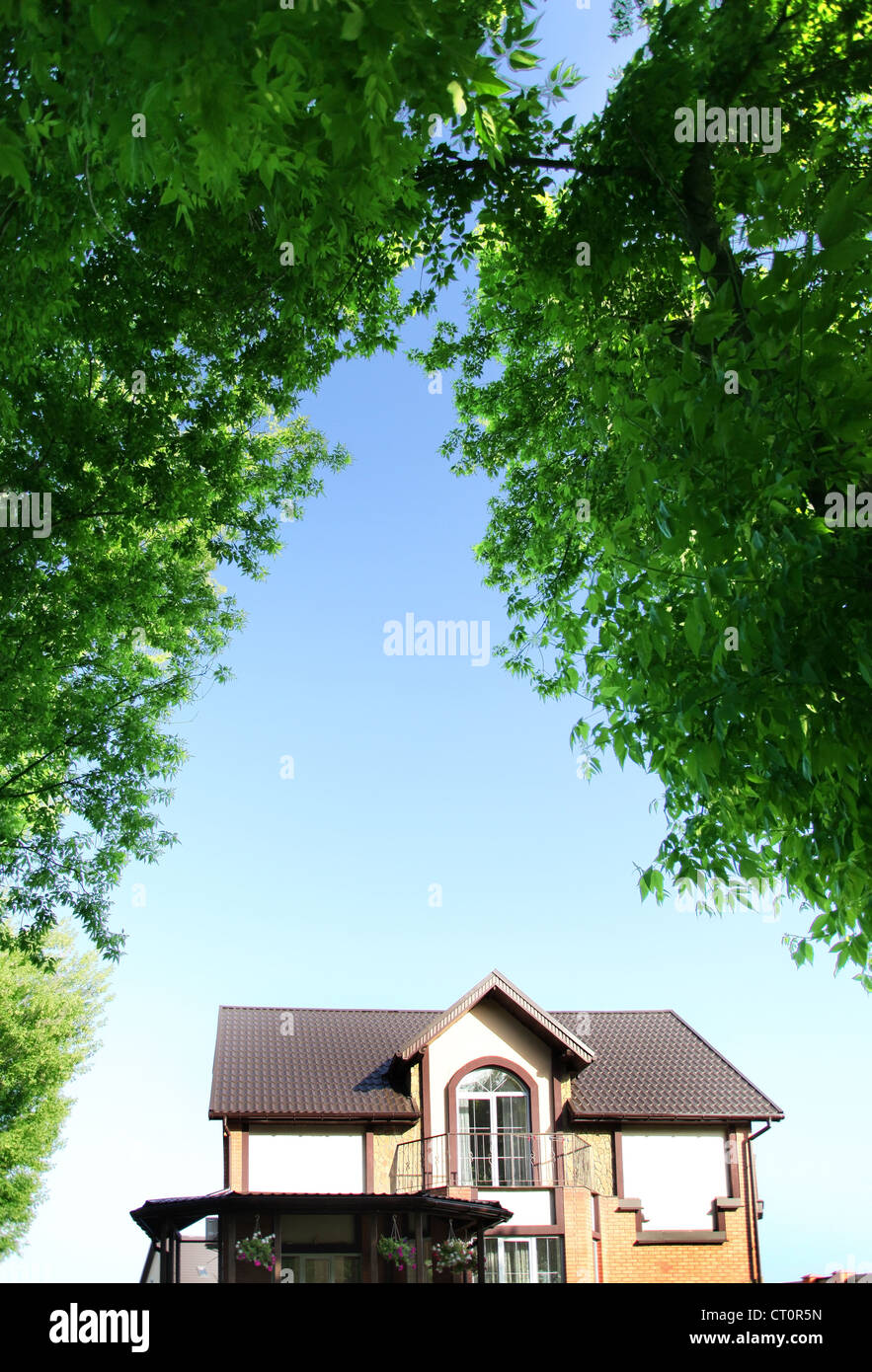 Bella casa sotto l'arco di alberi sullo sfondo del cielo estivo. Foto Stock