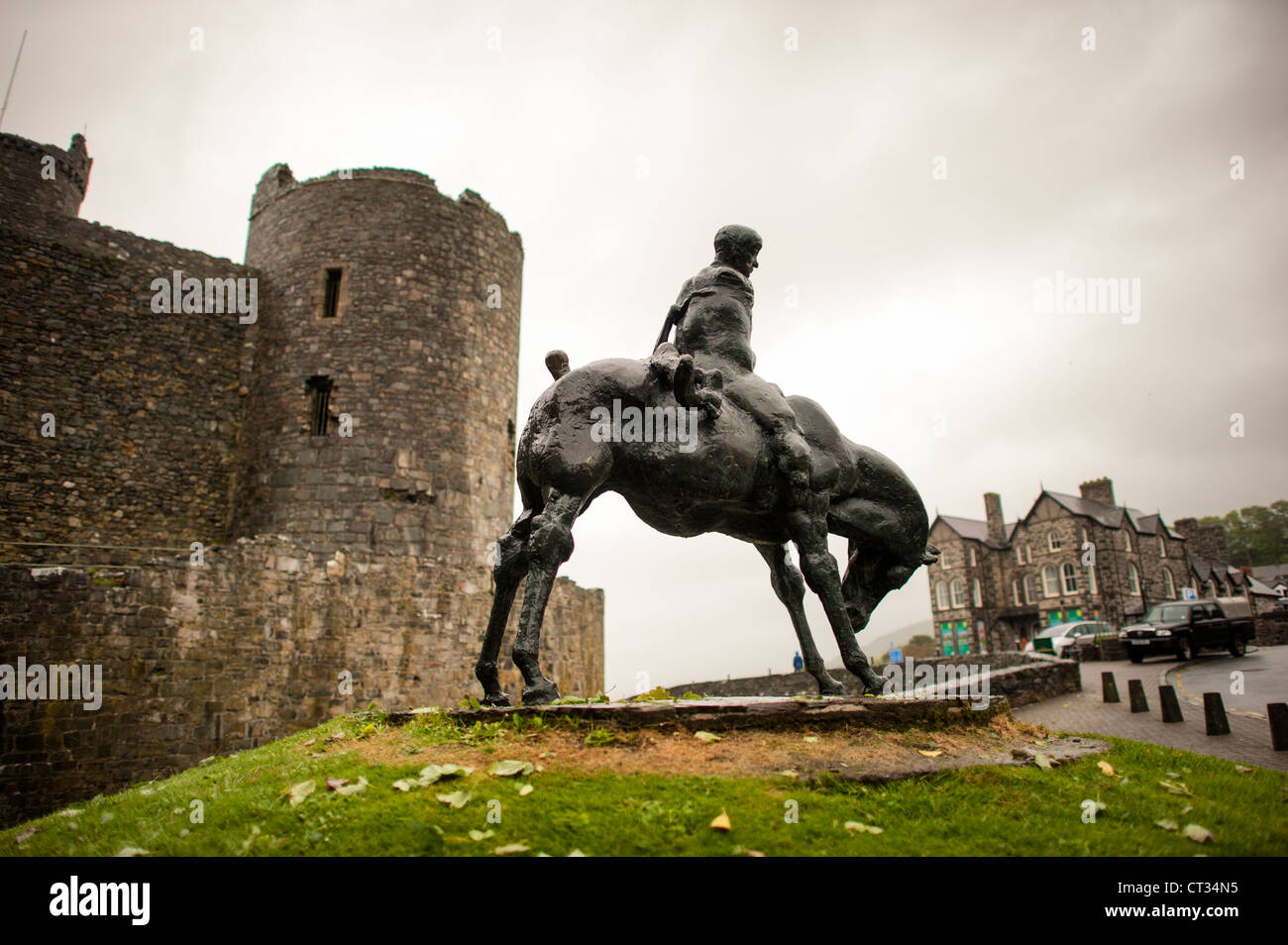 Statua dei Due Re Harlech Castle Scultura in bronzo Harlech Regno Unito | HARLECH, Galles — La scultura in bronzo I Due Re di Ivor Roberts-Jones del 1984 si erge davanti alle torri di pietra del castello di Harlech. L’opera raffigura il gigante Bendigeidfran che porta il bambino Gwern, una scena tratta dal ciclo mitologico gallese dei Mabinogion. La collocazione di questo monumento dedicato alla leggenda gallese nativa direttamente all’esterno di una fortezza costruita da Edoardo I tra il 1283 e il 1289 crea un contrasto deliberato con la storia di conquista inglese della regione. Foto Stock