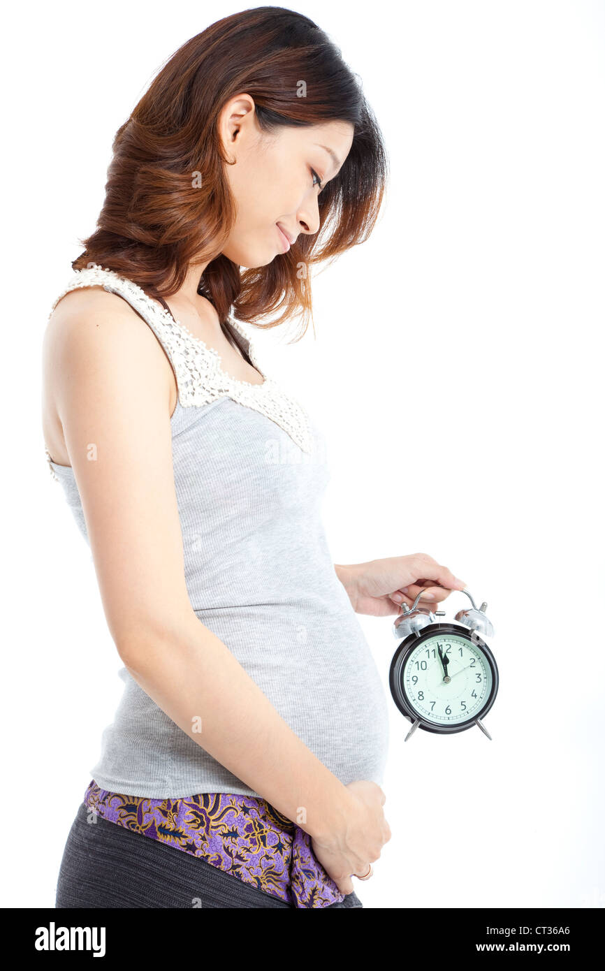 Asian donna incinta tenendo sveglia isolato su bianco Foto Stock