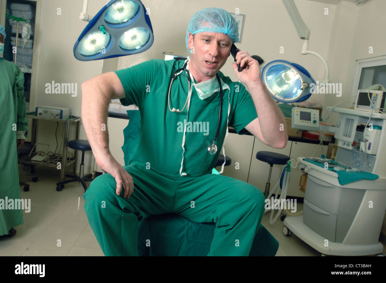 Un chirurgo ospedaliero seduto su un teatro operativo tabella, parlando sul suo telefono cellulare. Foto Stock