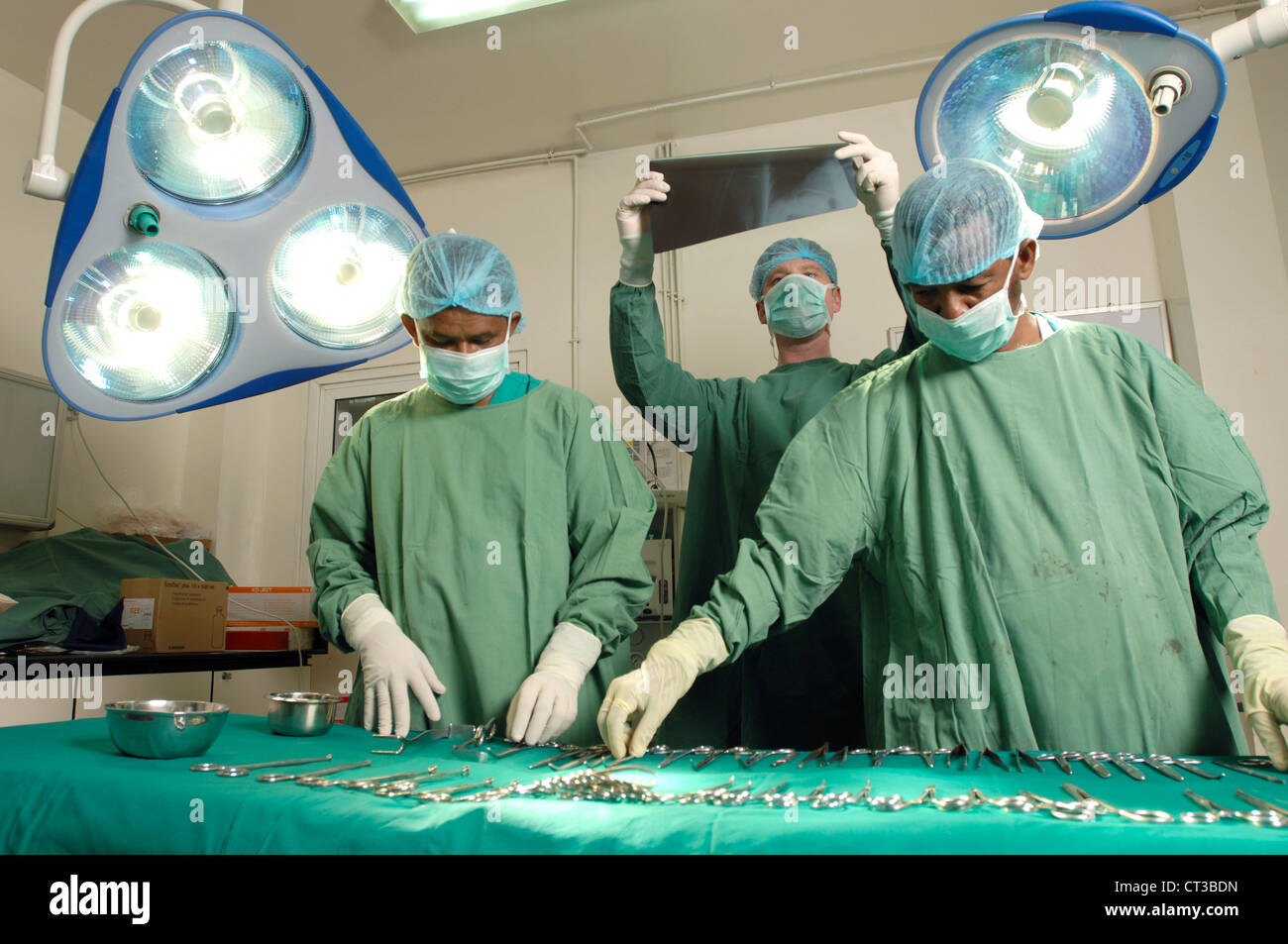 Un chirurgo esamina un x-ray mentre gli assistenti preparano gli strumenti chirurgici Foto Stock