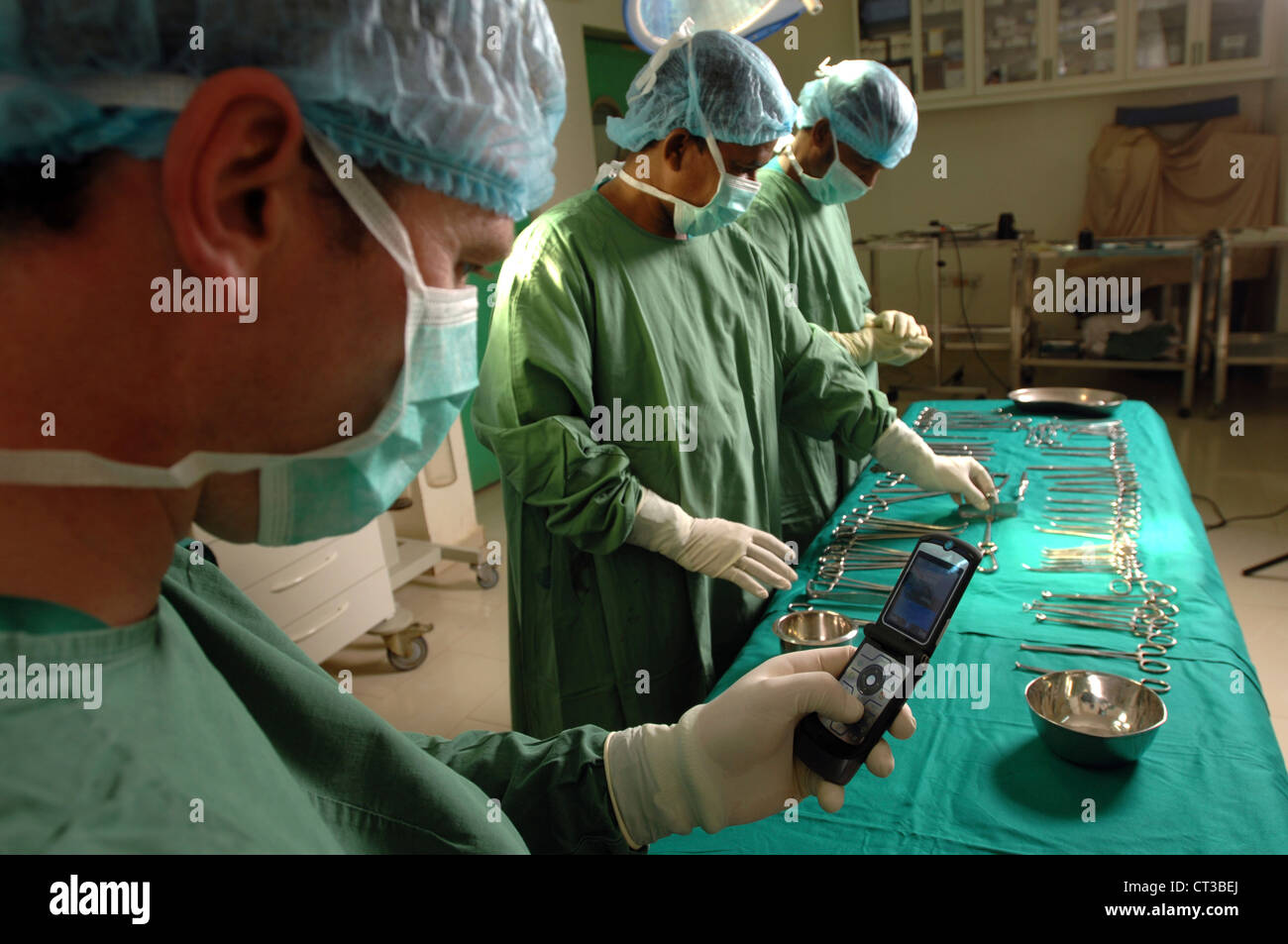 Teatro chirurgico personale posa vari strumenti chirurgici sul piano operativo mentre il chirurgo controlla il suo telefono cellulare. Foto Stock