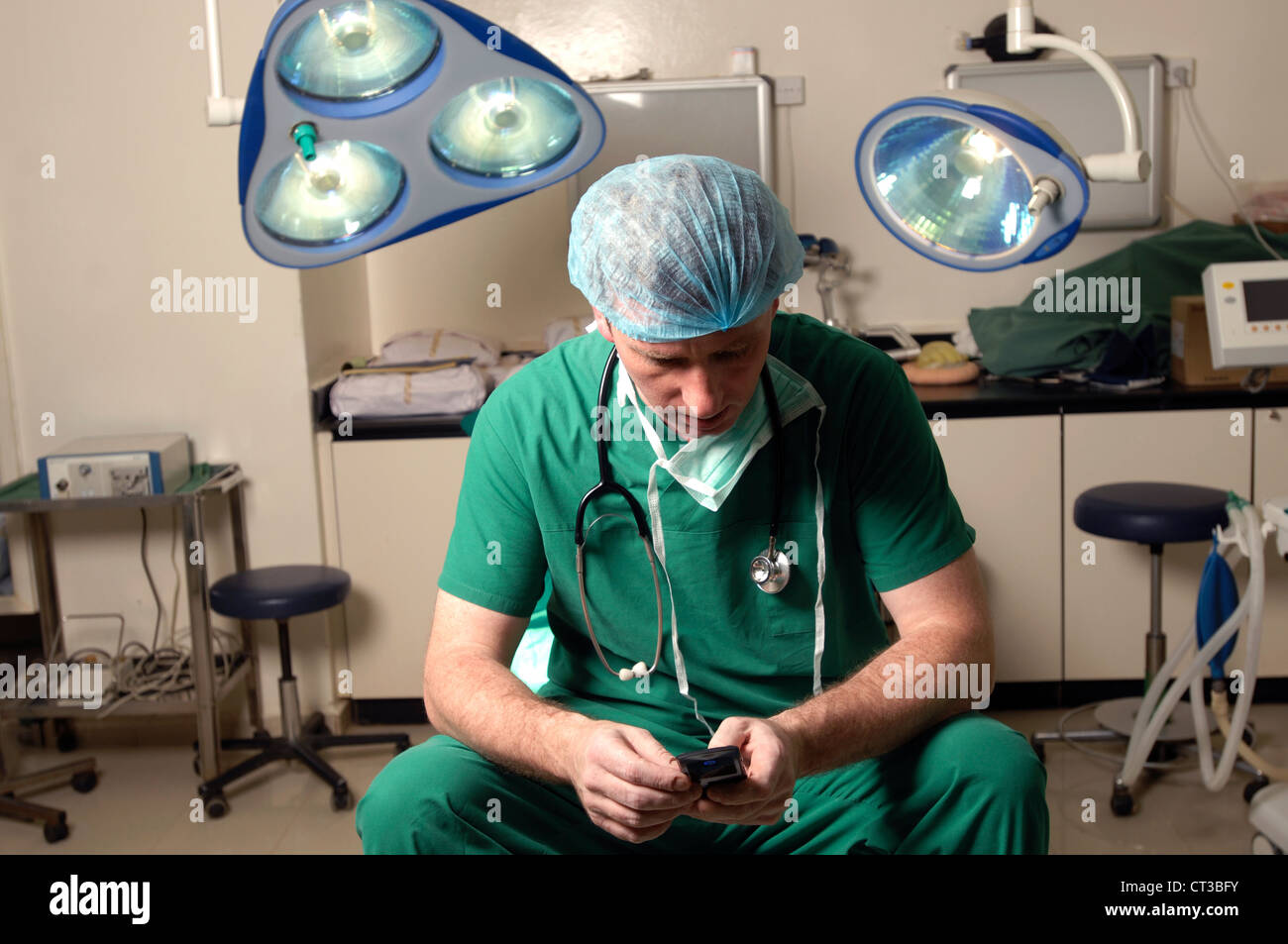 Un chirurgo seduto su un tavolo operatorio, utilizzando il suo telefono mobile. Foto Stock
