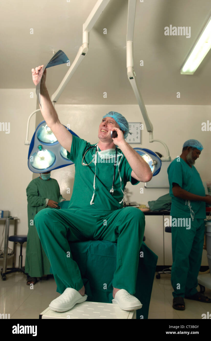 Un chirurgo occupato esamina un x-ray mentre si parla sul suo telefono cellulare Foto Stock