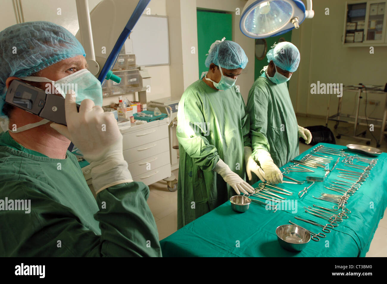 Teatro chirurgico personale posa vari strumenti chirurgici sul piano operativo mentre il chirurgo colloqui sul suo telefono cellulare. Foto Stock