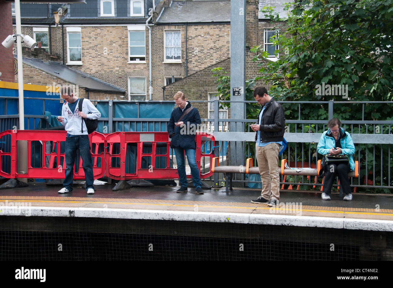 Quattro persone sulla piattaforma della stazione a Hackney Central, tutti guardando i loro telefoni cellulari Foto Stock